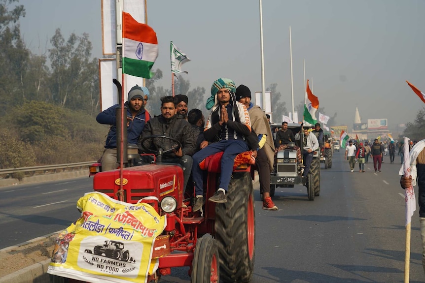 men on tractors bearing flags drive along the road alongside other men walking