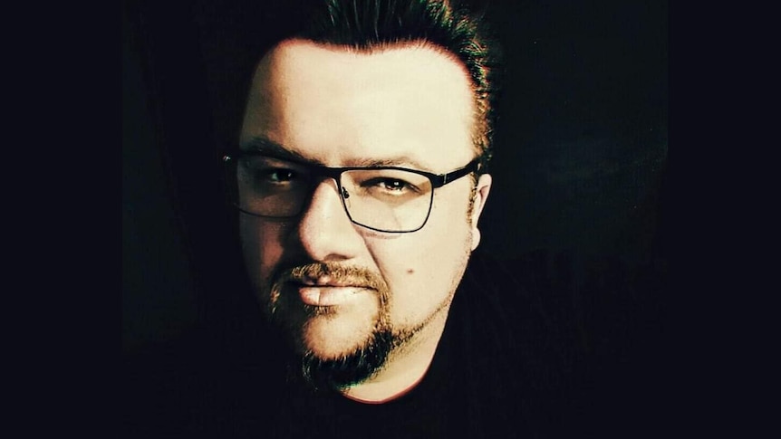 An edited photo of a man with glasses looking toward the camera with a black background.