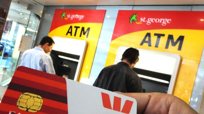 A person holds a Westpac account card in front of St George Bank ATMs