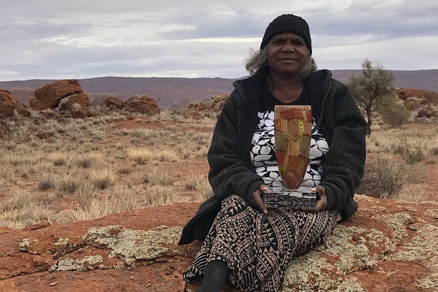 An artist sits on country holding her national indigenous art award