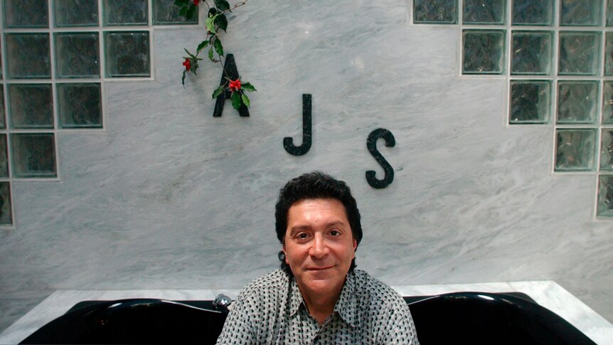A man sits in front of a wall with the letters A, J and S inscribed on it.