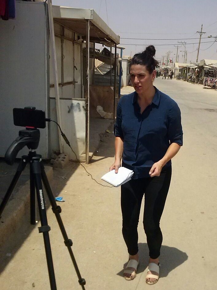 Video journalist Ashlynne McGhee crouching while filming her piece to camera at refugee camp in Jordan.