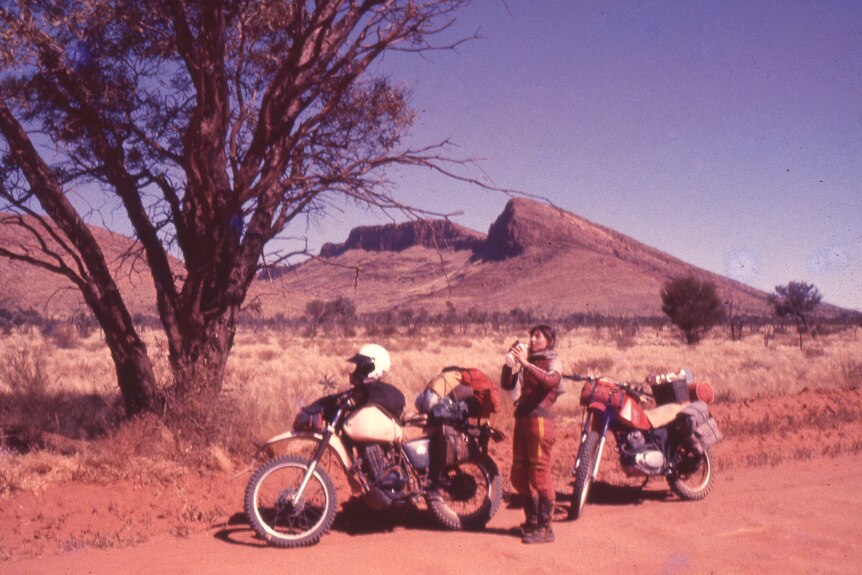 A woman pulled over on the side of a dusty highway with her motorbike.