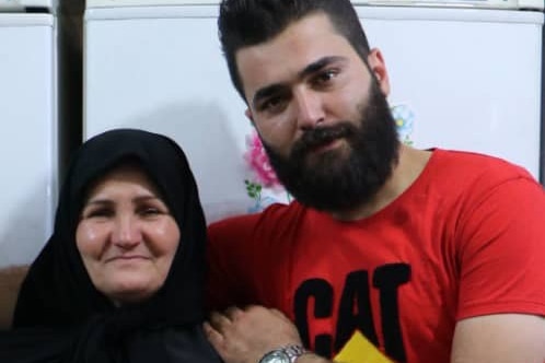 A smiling man in red tshirt hugs an older woman in a burkha