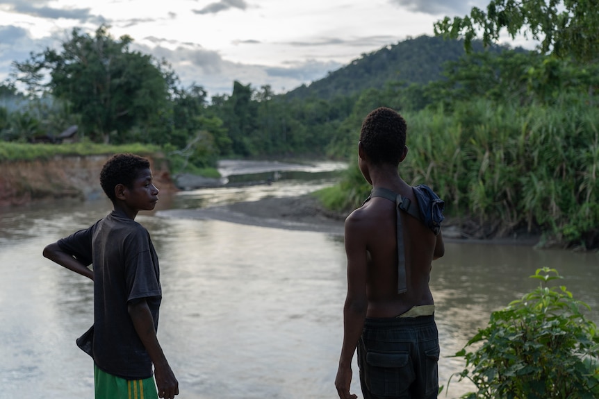 Boys stand near a river.