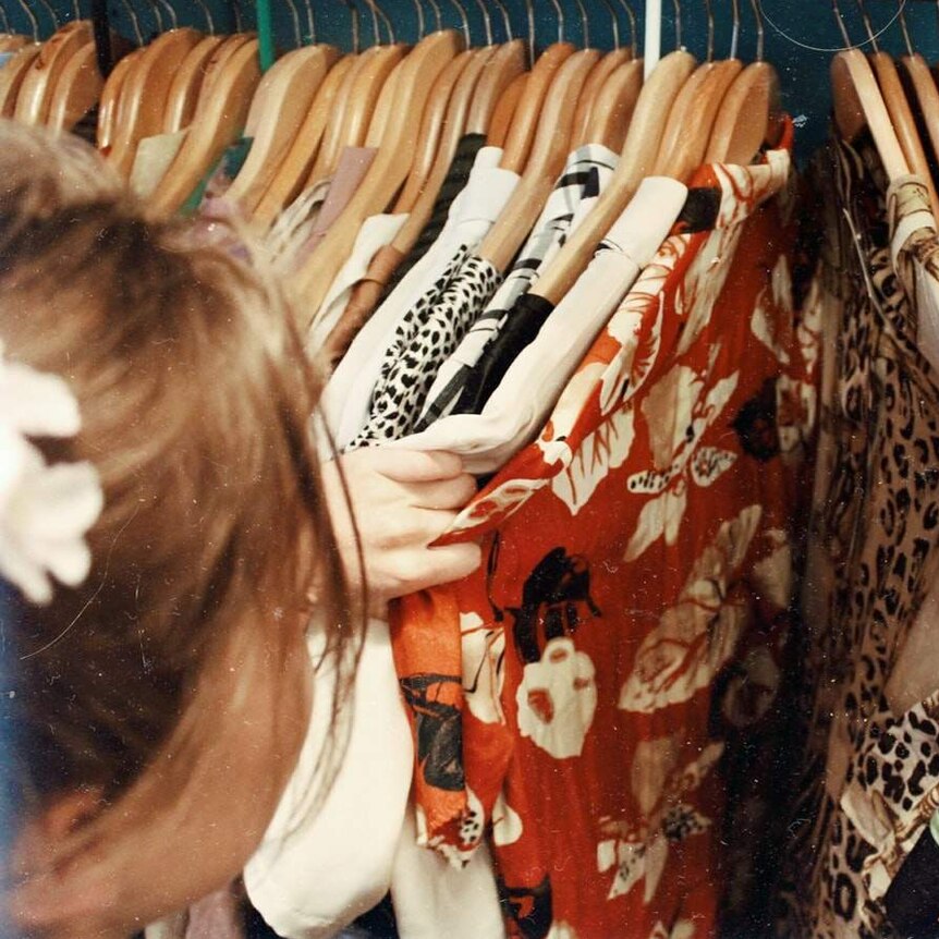 Woman sifts through clothing on rack.