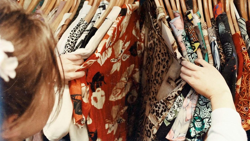 Woman sifts through clothing on rack.