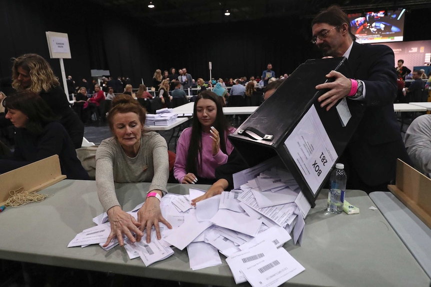 A man empties a box of ballots onto a table