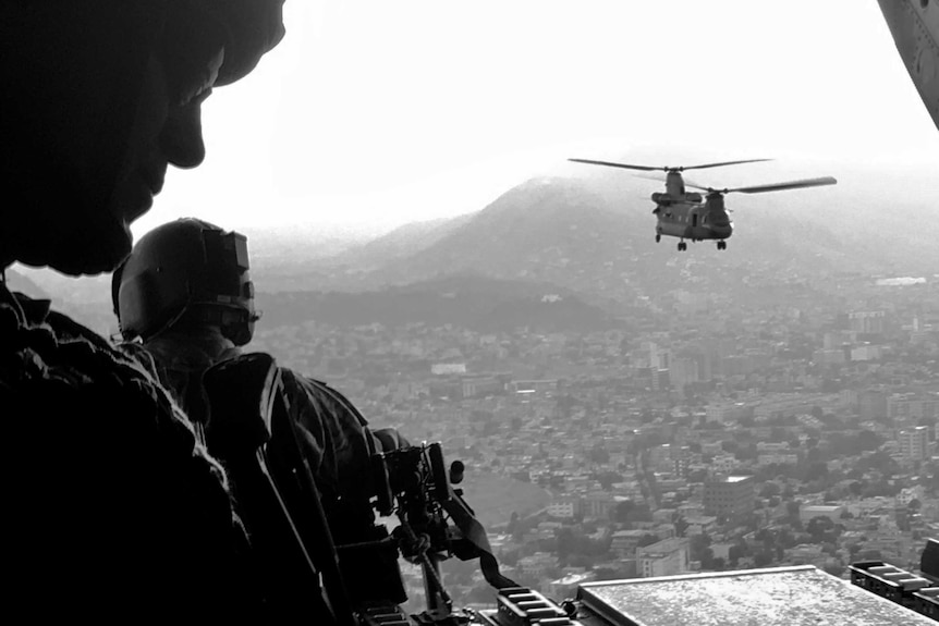 Profile shot of Speers looking out of helicopter with a twin rotor chopper in the distance in flight over city.