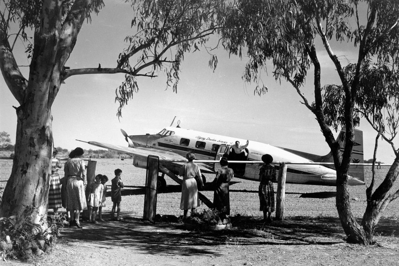 Flying Doctor being greeted by a group of waiting women and children, John Oxley Library, State Library of Queensland