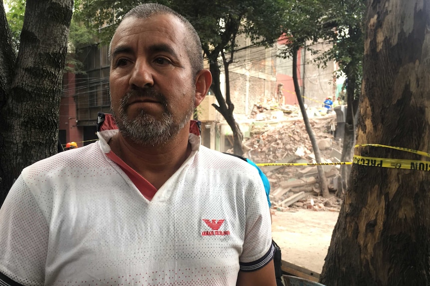Mexico City resident Francisco Ortiz stands in front of emergency tape and a collapsed building.