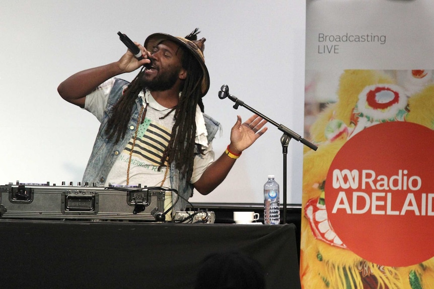 A man with dreadlocks sings into a microphone on a stage.