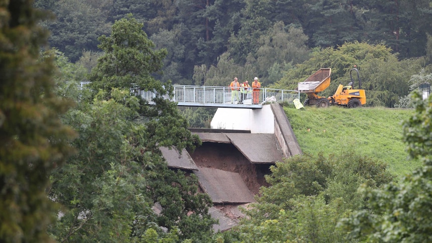 A team of men look at the damage to the wall of a dam.