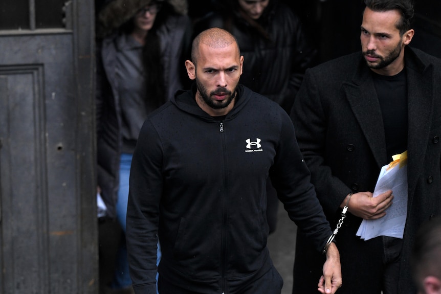 Two men wearing black clothing walk through a dark door with concerned looks on tehir faces. 