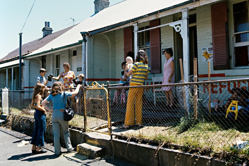 Women stand around the front of a small home in the 1970s.