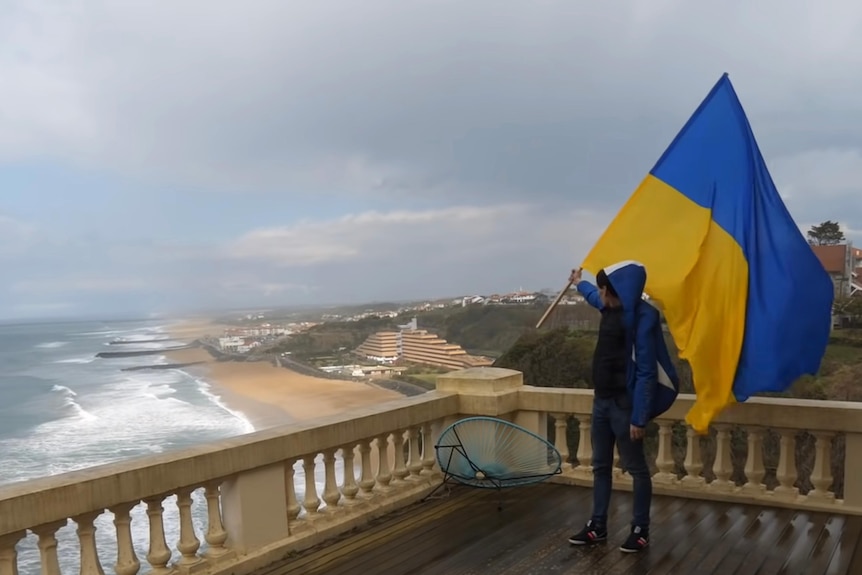一名活动人士在海边豪宅的阳台上举起乌克兰国旗。