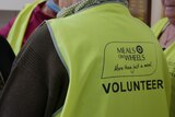 The back of a yellow hi-vest vest reads Meals on Wheels ... More than just a meal, VOLUNTEER