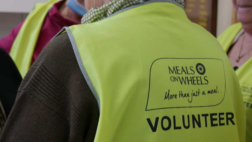 The back of a yellow hi-vest vest reads Meals on Wheels ... More than just a meal, VOLUNTEER