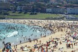 A packed Bondi beach is filled with swimmers in the ocean and sunbakers on the sand.