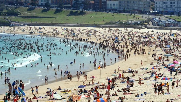 A packed Bondi beach is filled with swimmers in the ocean and sunbakers on the sand.