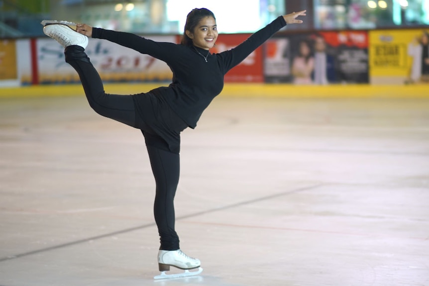 Nurul Ayinie Sulaeman smiling while she figure skates on one leg with her arms outstretched.