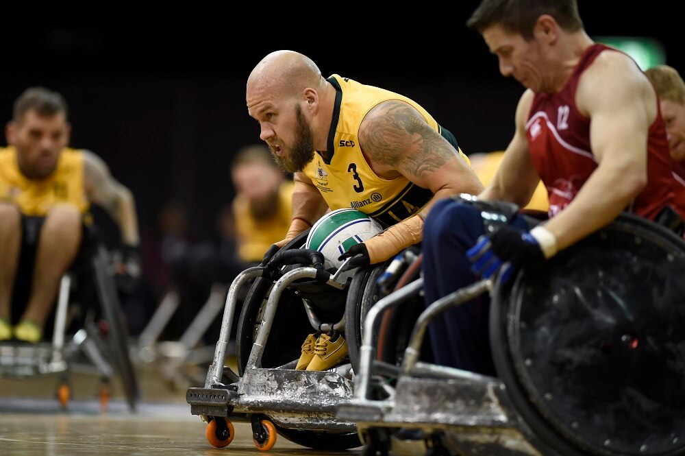 Male athlete in wheelchair holds rugby ball as he prepares to dodge other players 