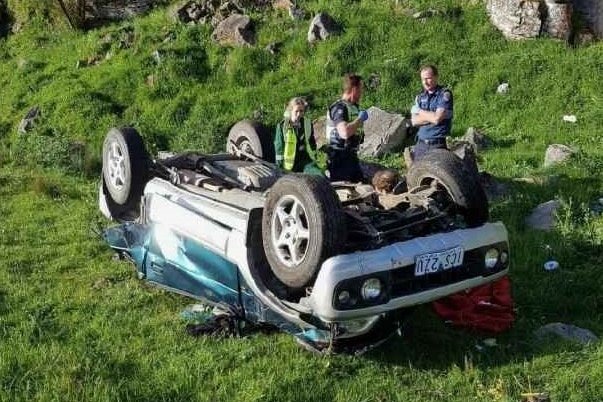 a car after it has plunged 50m down a cliff and is lying upside down with emergency services looking on