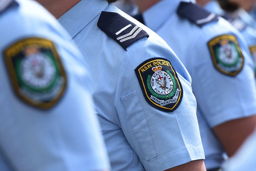 A group of police officers line up side by side. Only their uniformed shoulders are visible.