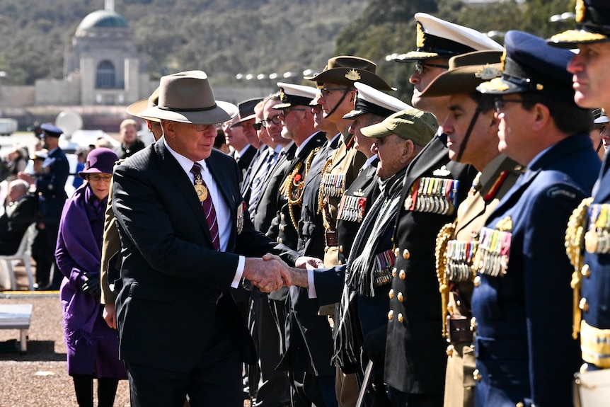 A row of military personnel shakes hands with Sir David Hurley, the War Memorial in the background.