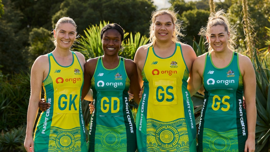 Four Australian team netballers stand together in a garden wearing team uniforms with an Indigenous pattern on them. 