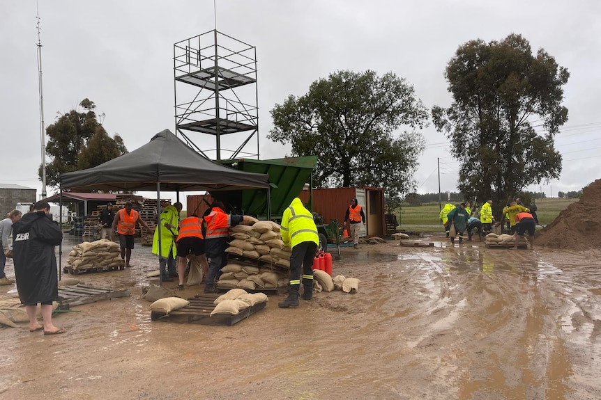 several people wearing hi vis rain jackets pile up sand begs under a pop up gazebo