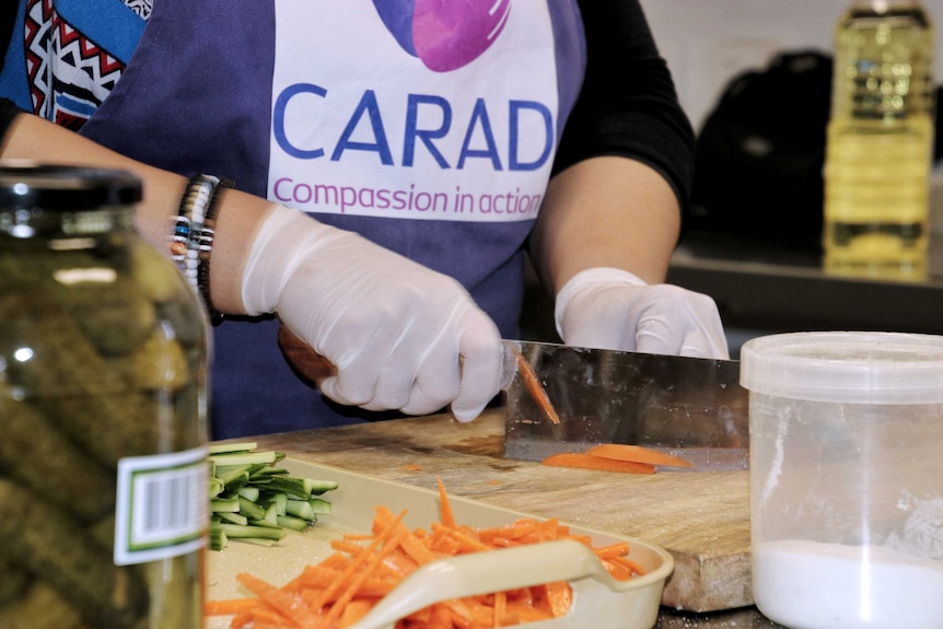 A close-up shot of Fadhaa Al-Khalidi's hands as she chops carrot with a large knife wearing rubber gloves.