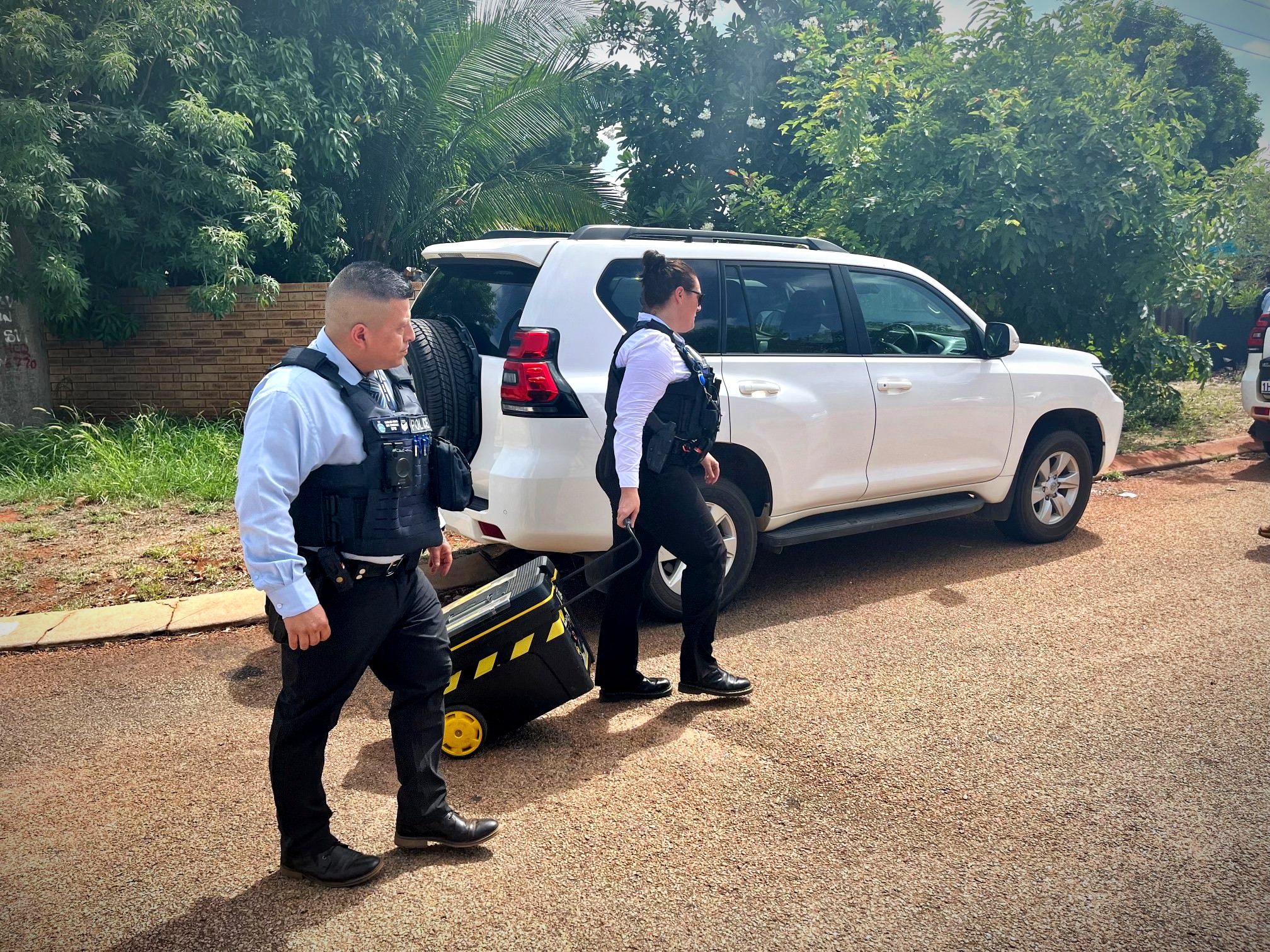 Police remove a black and yellow suitcase from a home