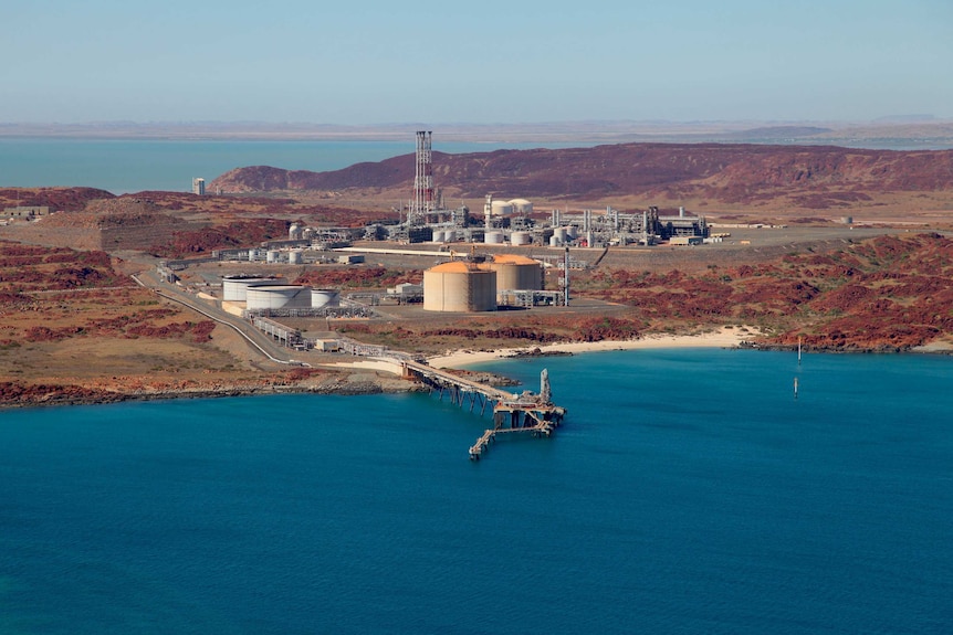 Turquoise ocean, red rocks and machinery and docks extending into the waters.