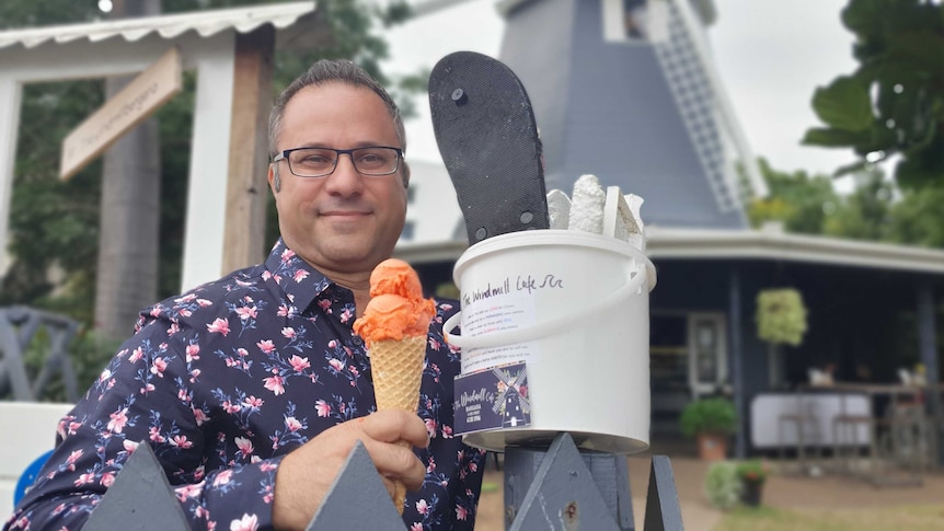 A man holding a bucket of rubbish in one hand and a gelato in the other.