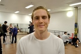 A man stands smiling in a rehearsal room at a dance studio.