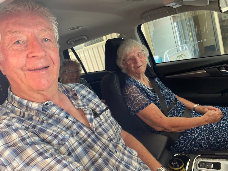 three people sit in a car, a man is in the drivers seat and two elderly women sit in the passenger and back seat