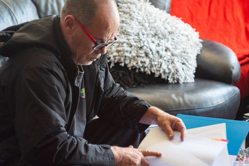 A man with glasses looks at a folder full of documents.