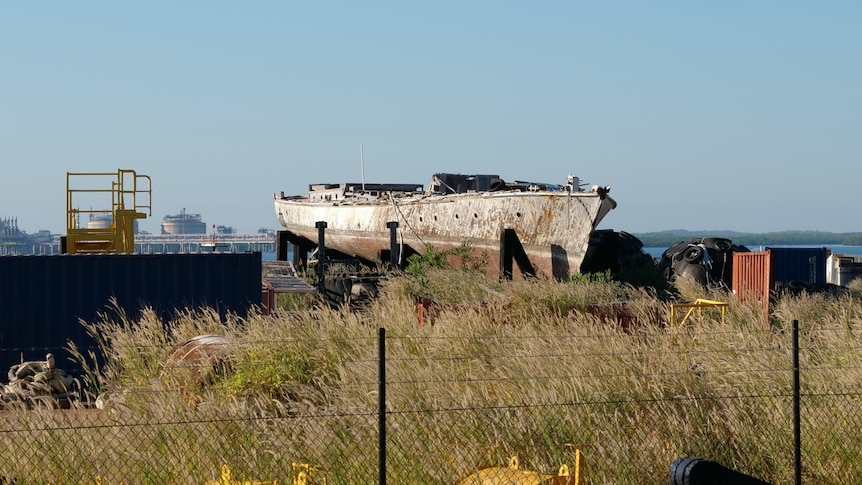 A sorry-looking 24m wooden motor boat on a cradle in an industrial port area.