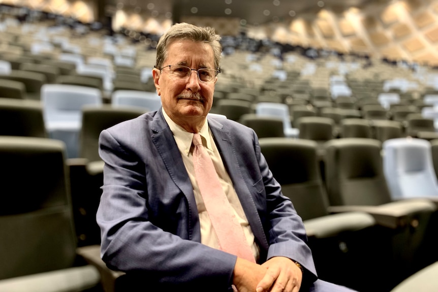 A man sits in an auditorium with empty seats behind him