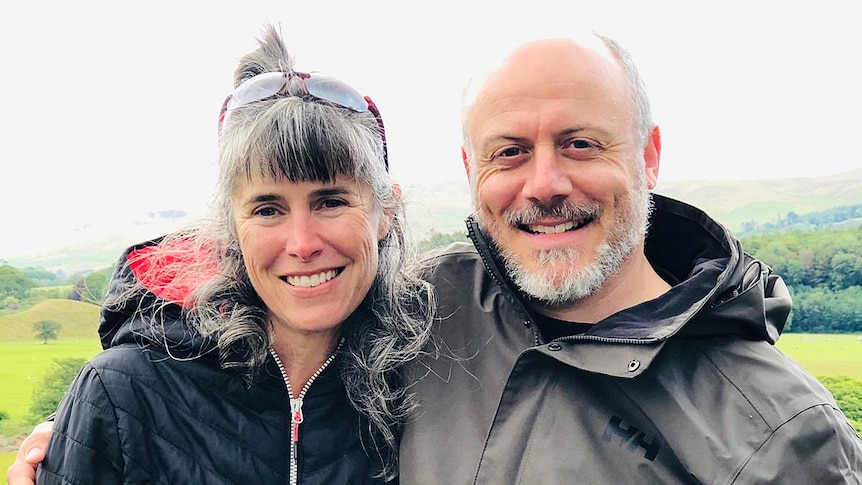 A woman and man stand outside with their arms around each other