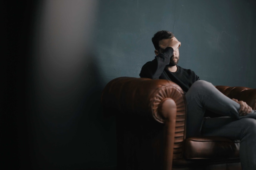 A man sitting on a couch holds his head.