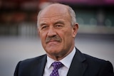 MCU of Wally Lewis wearing dark suit, white shirt and purple tie