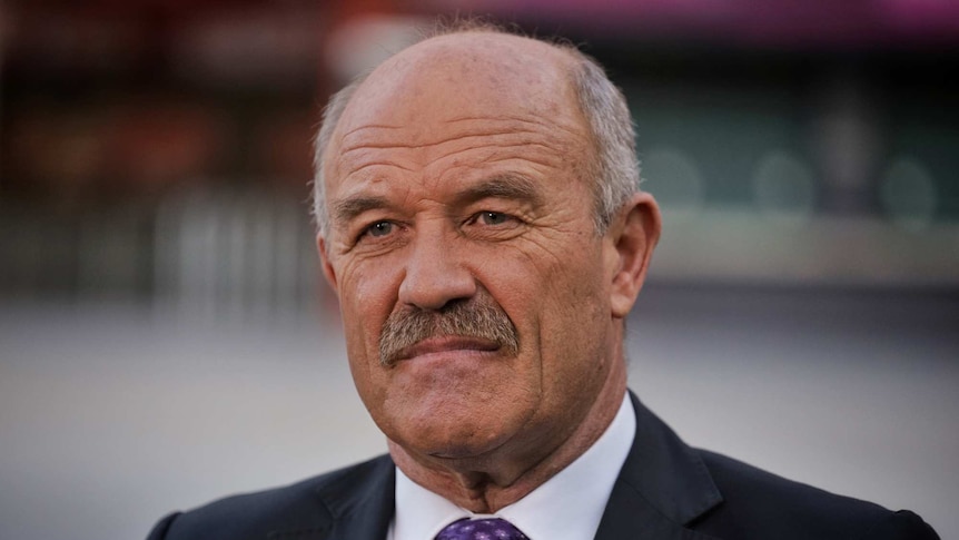 MCU of Wally Lewis wearing dark suit, white shirt and purple tie