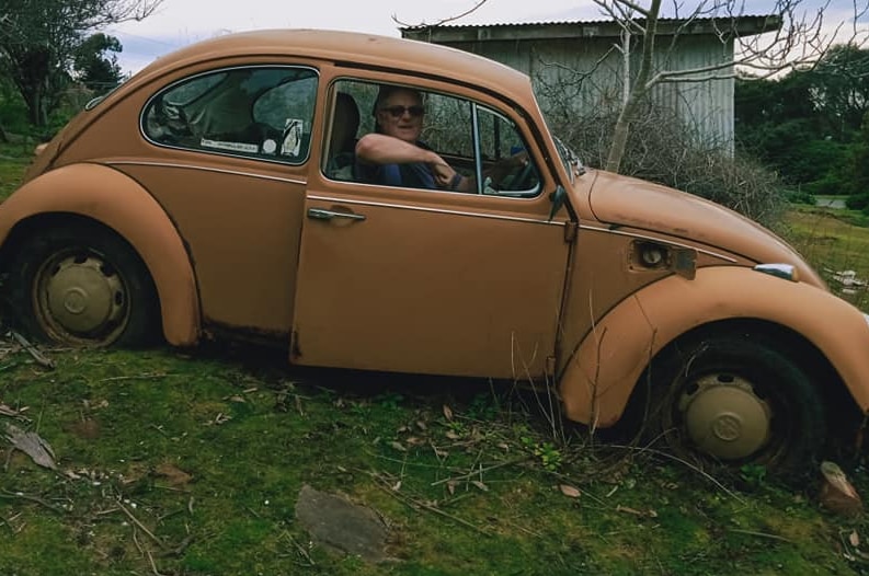 Wide shot of a man in an old car in a paddock