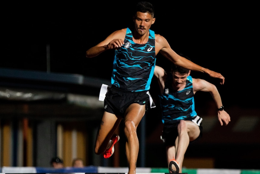 Matthew Clarke goes over the water jump in a steeplechase race, with Max Stevens right behind him.