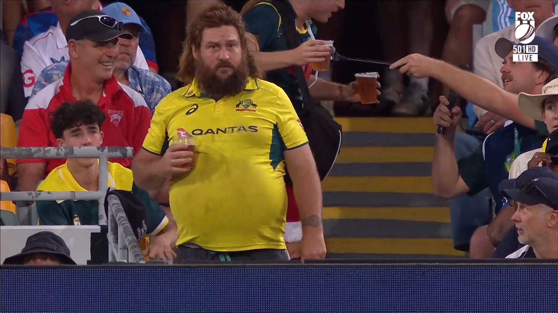 Un hombre con una camisa amarilla y un salmonete sostiene una cerveza en la mano en medio de una multitud.