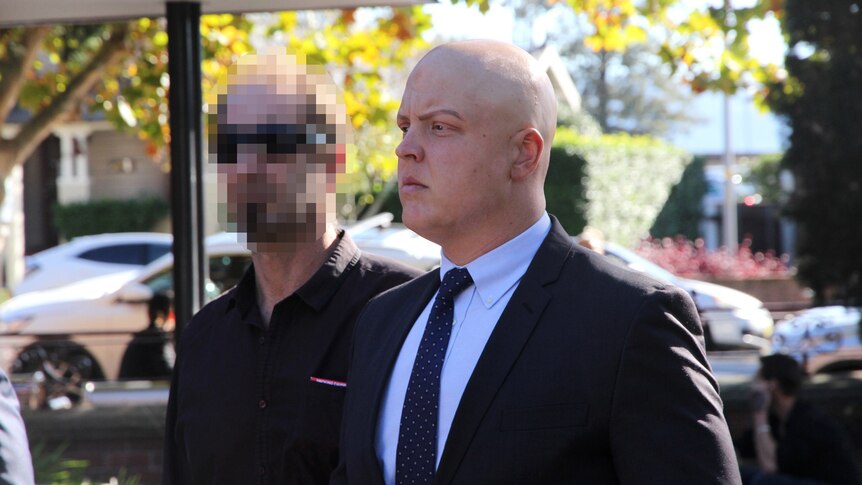 A bald man in a suit next to a man with a pixelated face.