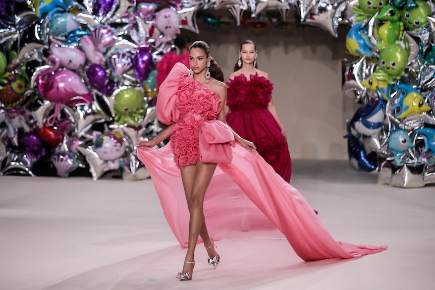 Two models dressed in two shades of pink in front of a balloon arch. 