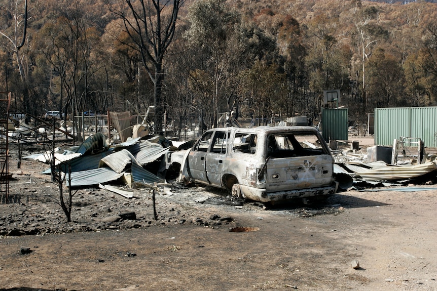 Ruins of a house completely destroyed by a fire and a burnt out car on charred ground. 